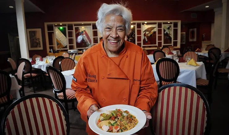 Leah Chase sitting at a table with a plate of food