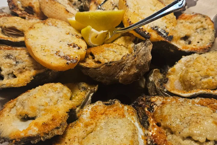 Plate of grilled oysters topped with bread and lemon wedges.