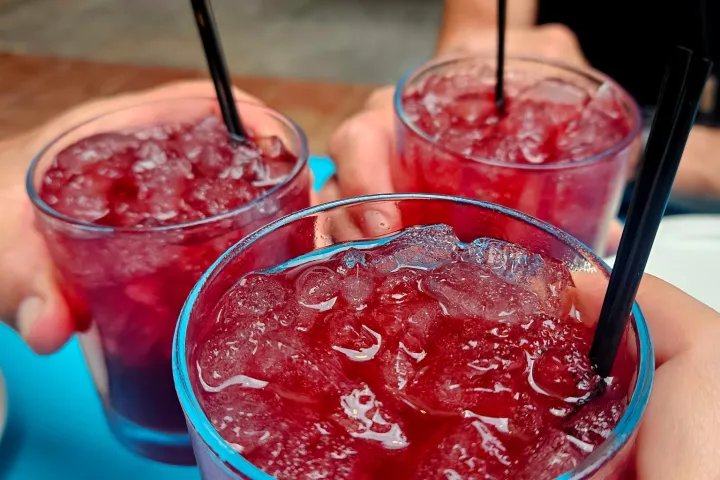 Three hands holding glasses of iced red drinks with black straws.