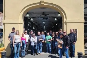 Group of people posing under 'French Market' archway on a sunny day.