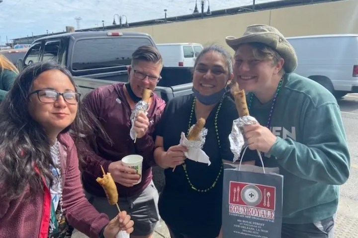 Four people smiling and holding wraps outdoors near parked vehicles.