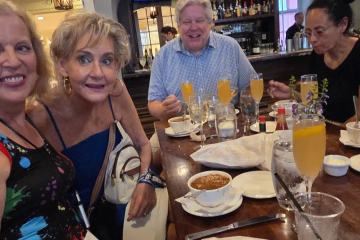 Four people smiling at a restaurant table with drinks and desserts.