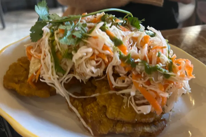 Plantain tostones topped with shredded cabbage, carrots, and herbs on a white dish.