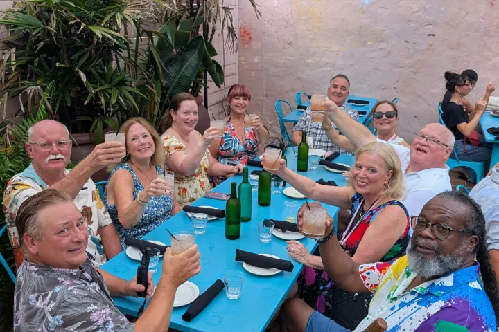 Group of people sitting around a table outdoors, raising glasses and smiling.