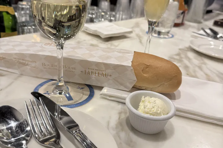 Table setting with wine, bread, butter, and a cocktail at a restaurant counter.
