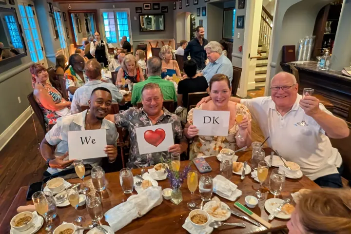 Group of people holding signs at a restaurant table with drinks and desserts.