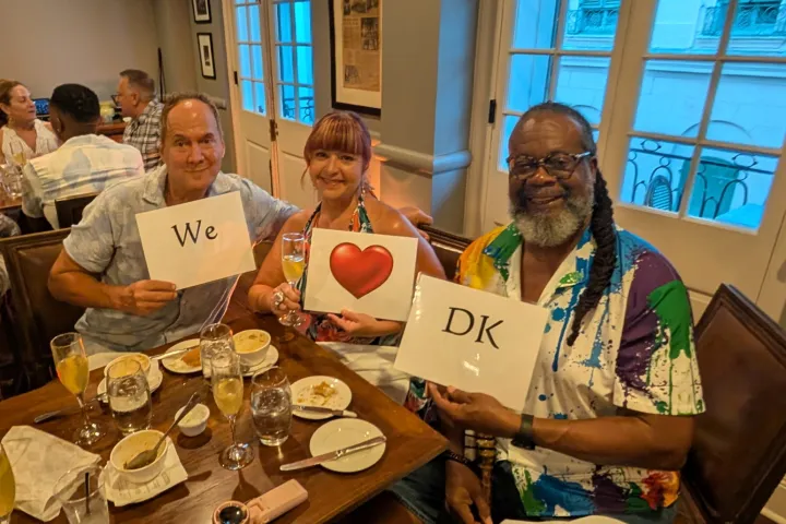 Three people in a restaurant holding signs reading 'We ❤️ DK'.