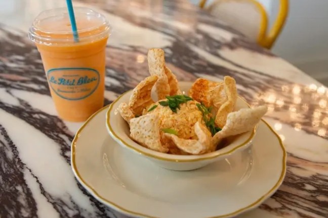 Chips in a bowl on a marble table, next to a smoothie with a blue straw.