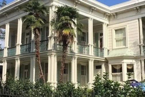 Elegant white mansion with columns and palm trees in front.