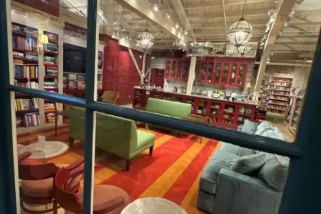 Cozy library with colorful sofas, bookshelves, and hanging lamps viewed through a window.