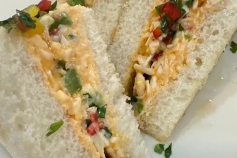 Three triangular sandwiches with colorful vegetable and cheese filling on a white plate.