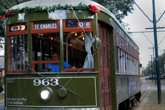 Green St. Charles streetcar in motion, decorated with wreath, on a track lined with trees.