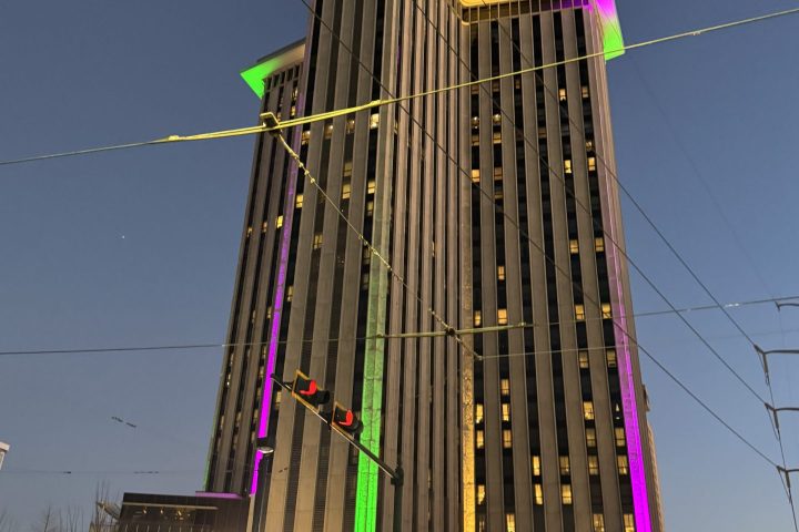 Tall building with neon green and purple roof lights at dusk.