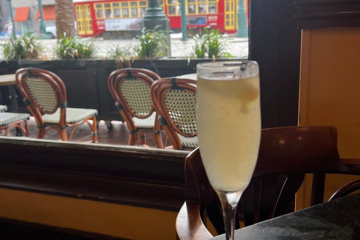 Tall glass of champagne on table, red streetcar visible through window.