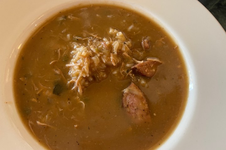 Bowl of gumbo with rice and meat chunks in brown broth on white plate.
