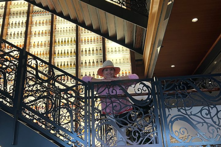 Person in striped shirt and hat on ornate staircase with bottle display in the background.