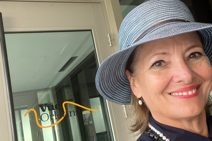 Woman in a blue hat smiling near a glass door with 'Vue Orleans' visible.