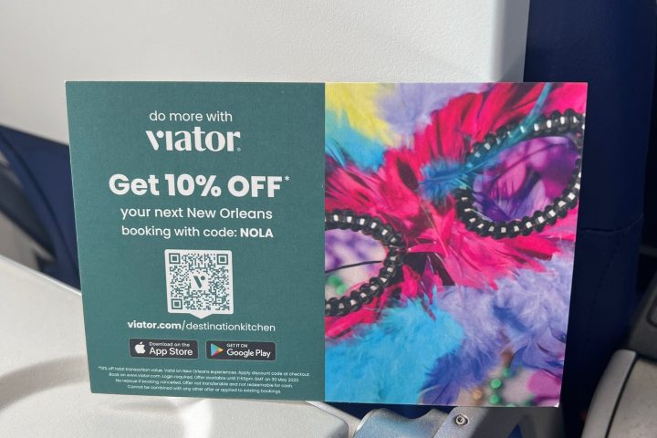 Flyer on airplane tray table offering 10% off New Orleans bookings with vibrant mask and feathers design.