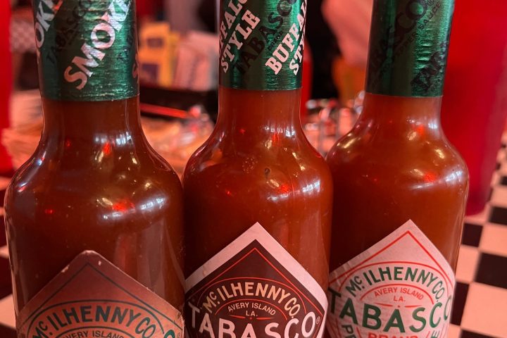 Three Tabasco sauce bottles on a checkered table in a dimly lit restaurant.