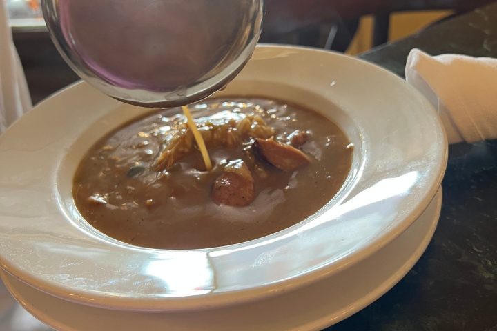 Ladle pouring hot liquid into a bowl of soup with visible chunks on a table.