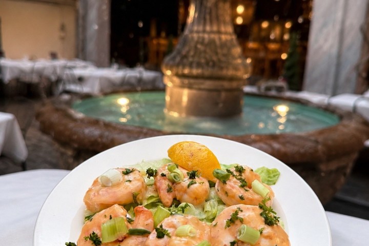 Shrimp salad on a plate in front of an ornate fountain.