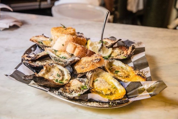 Plate of grilled oysters with bread and lemon on a marble countertop.