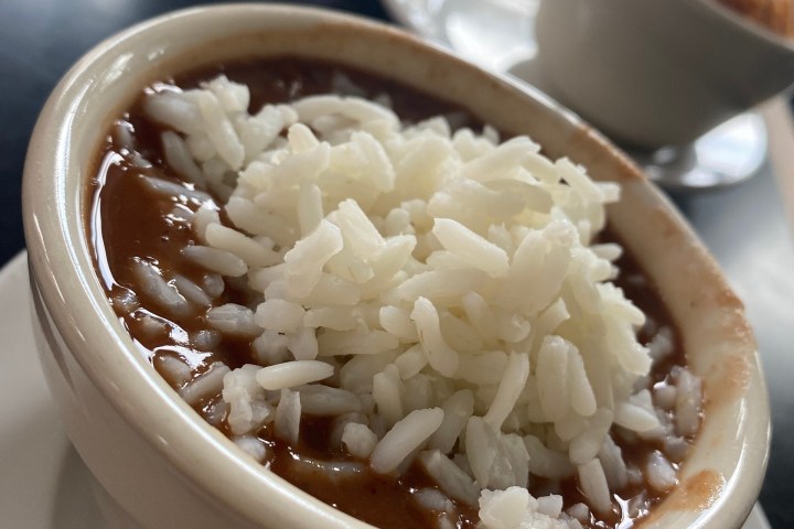 Bowl of chili topped with rice on a table with another dish in the background.